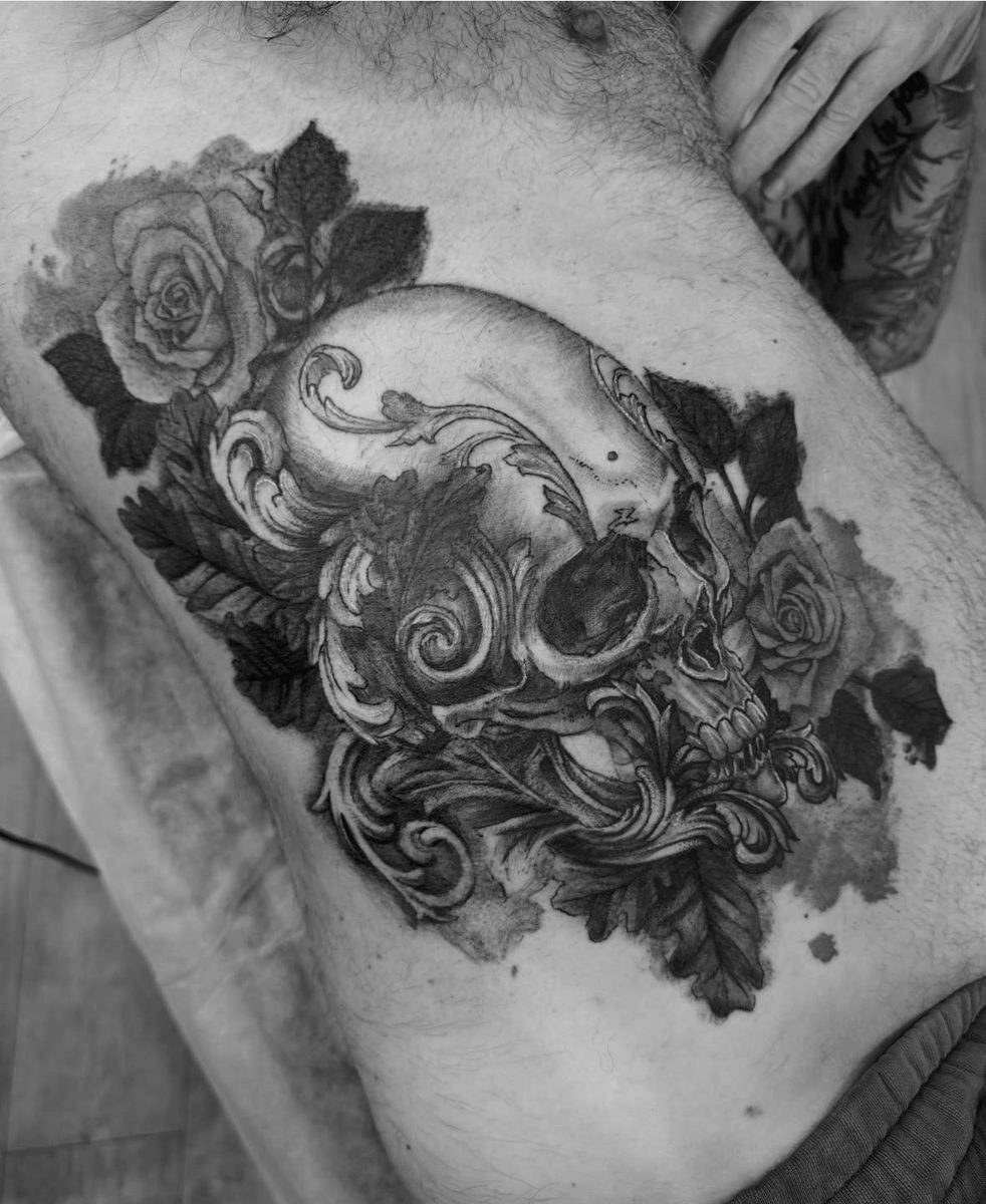 Ornate skull and rose tattoo on torso in illustrative blackwork by Charlie Lund