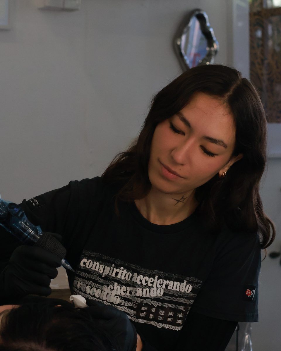 Portrait of Izzy Antonievich, illustrative tattoo artist at Prana Tattoo, working at the window of the studio